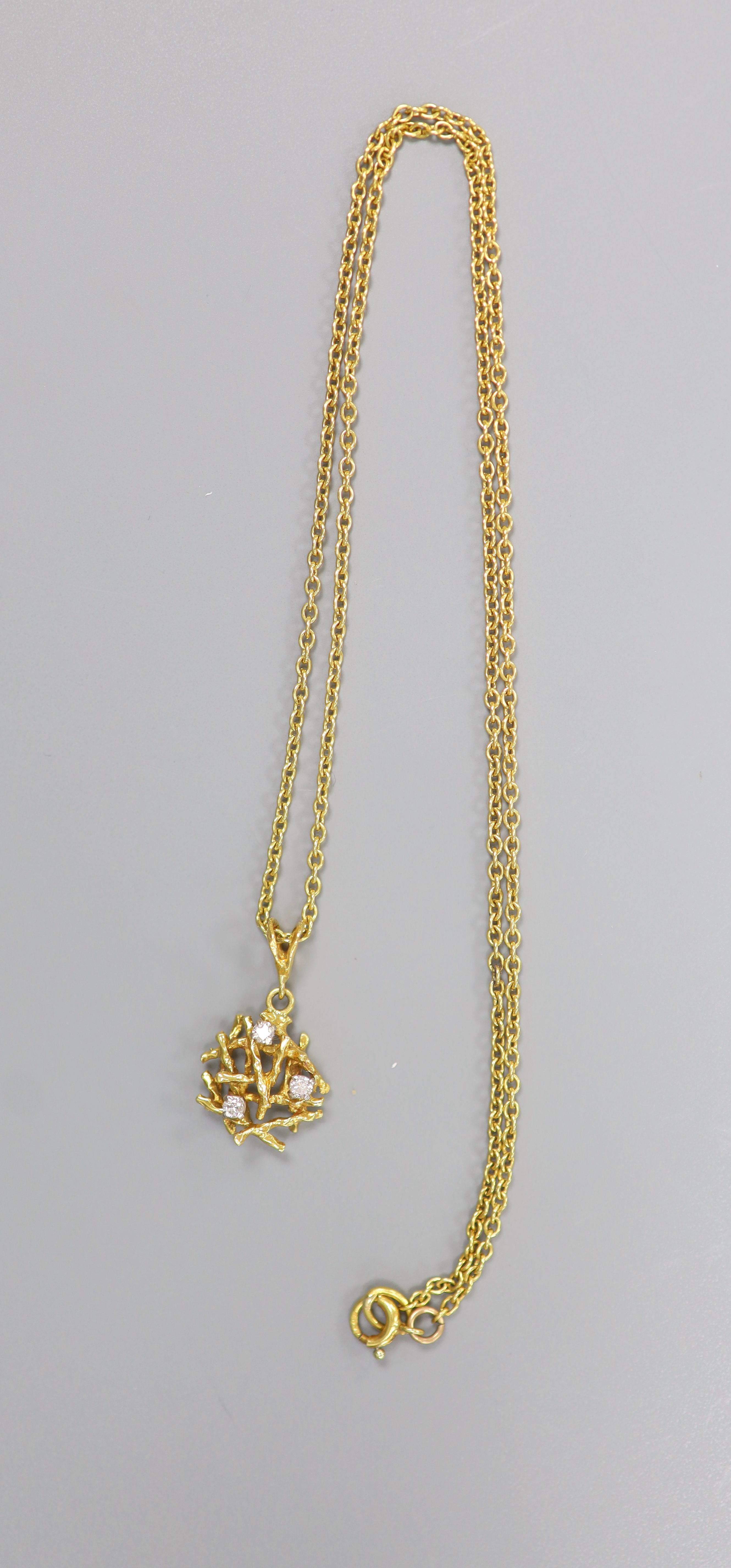 A modern yellow metal and three stone diamond set rustic pendant, 15mm, on a 18ct chain, 45cm